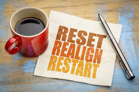 A cup of coffee, a pen, and a napkin with the words 'RESET REALIGN RESTART' printed on it, placed on a wooden surface.