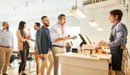 A group of customers waiting in line at a coffee shop, with a barista at the counter serving one of them.