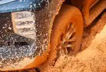 Close-up of a muddy tire stuck in dirt, highlighting the vehicle's wheel and mud splatter.