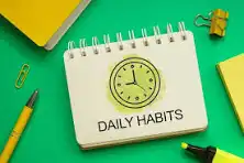 A notepad with the text 'DAILY HABITS' and a clock illustration, surrounded by stationery items on a green background.