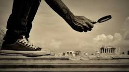A hand holding a magnifying glass, positioned above a miniature landscape featuring a historical building, with a sneaker-clad foot in the foreground.
